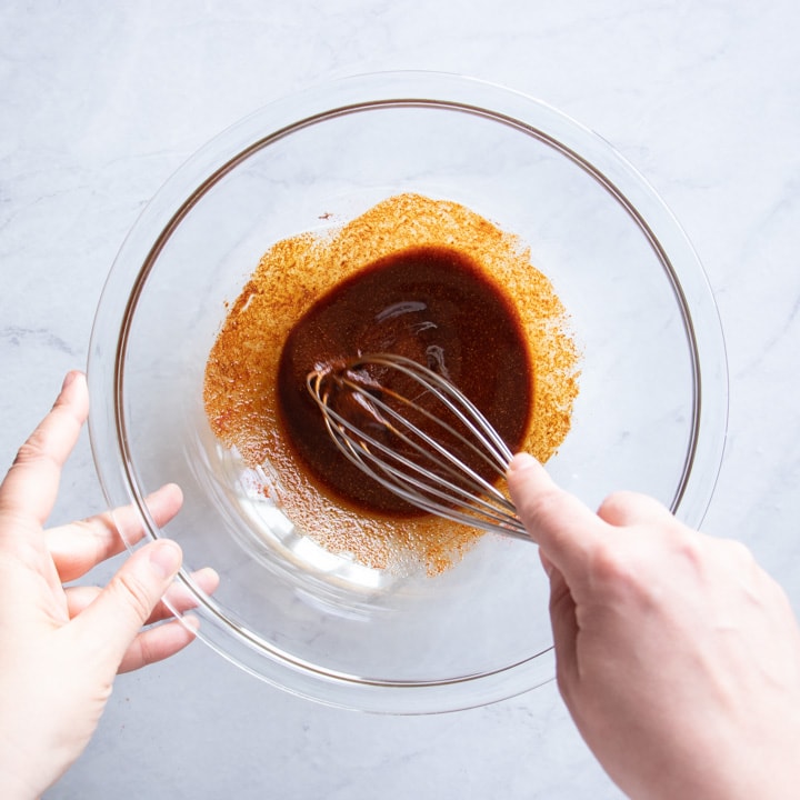 Whisking a Moroccan chicken marinade in a glass bowl.
